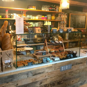 A glass sneeze guard in a cafe with cakes, bread and other products on top of and behind the screen.