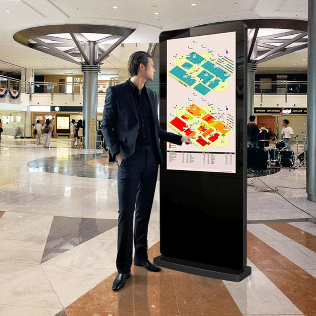 A man using a black interactive digital touch screen totem in a shopping mall.