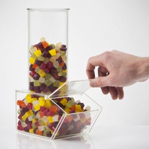 An acrylic sweet dispenser full of colourful sweets with a hand reaching in lifting the lid of the sweet dispenser.