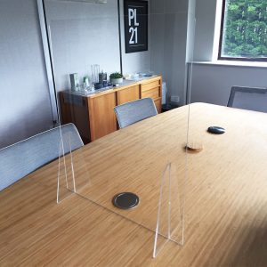 A clear acrylic desk sneeze guard sat on a table in an office.