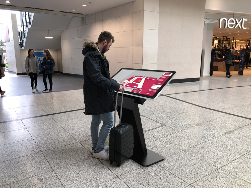 A windows touch screen kiosk in a shopping mall with a man using it.
