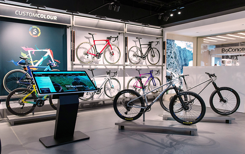 A windows touch screen kiosk with bicycle information on it, in front of a bike display in a shop.