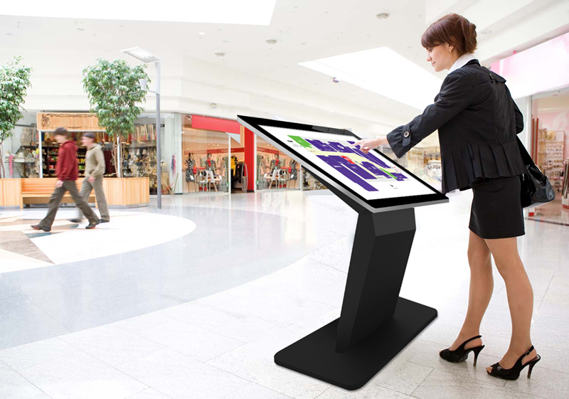A windows touch screen kiosk in a shopping mall with a lady using it.