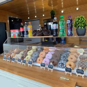 Sneeze guard food screen cover in a café with donuts, cakes and drinks in and on top of the sneeze guard.