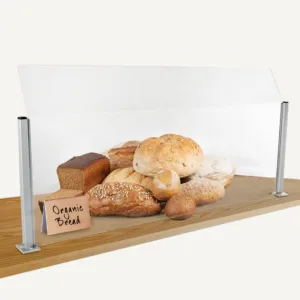 A counter sneeze guard with bread behind it and a wooden sign.
