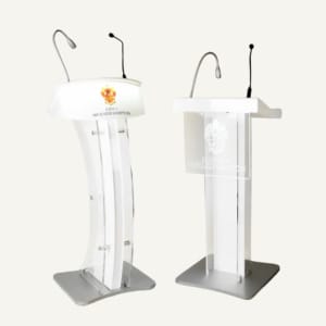 Two acrylic lecterns with silver and black microphones and logos on the front of them.