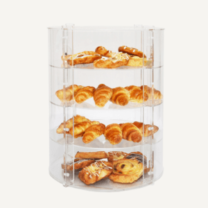 A clear acrylic circular display case with a selection of pastries on the four shelves.