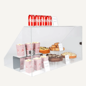 A clear acrylic sneeze guard with different food products inside and drink cans on top.