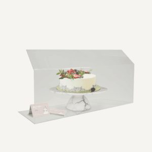 A hygienic sneeze guard with a cake sat behind it.