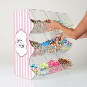A clear acrylic wedding pick and mix bin with custom pink and white striped printing on the side panels with "Mr & Mrs" on the side, and a hand reaching in to scoop some sweets.