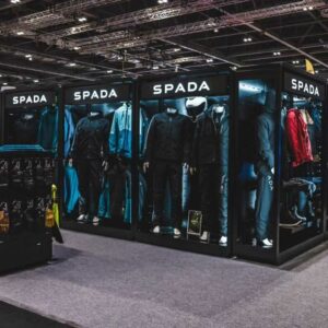 A wide corner angle of a Feridax Spada exhibition retail display, showcasing mannequins, clothing, motorbike helmets and shoes under lighting.