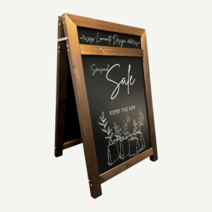 A wooden A-board chalkboard with a header with seasonal sale promotional hand drawn in white chalk.