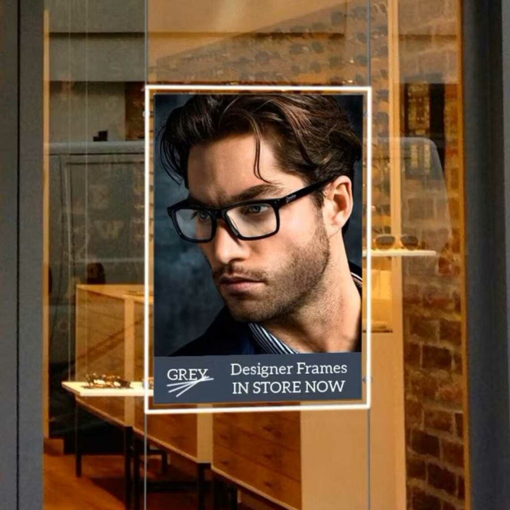 A LED window pocket frame advertising some glasses on a man in front of an opticians.