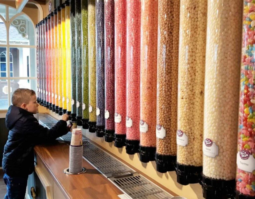 A young boy looking at a wall full of colourful pick and mix dispensers with different sweets inside.