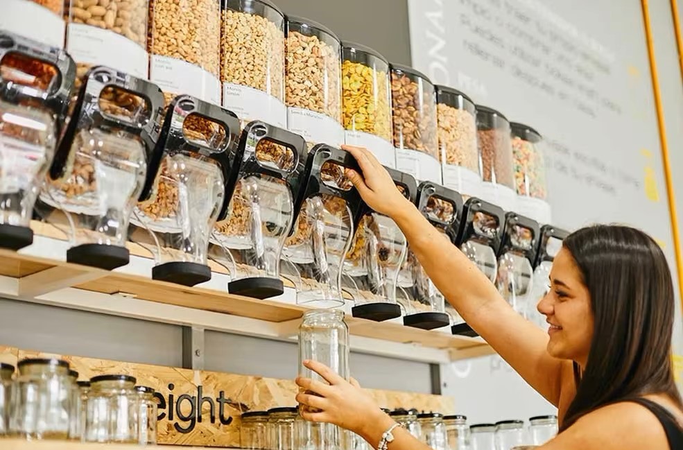 A lady using a wall mounted dry food dispenser with different cereals and nuts inside.