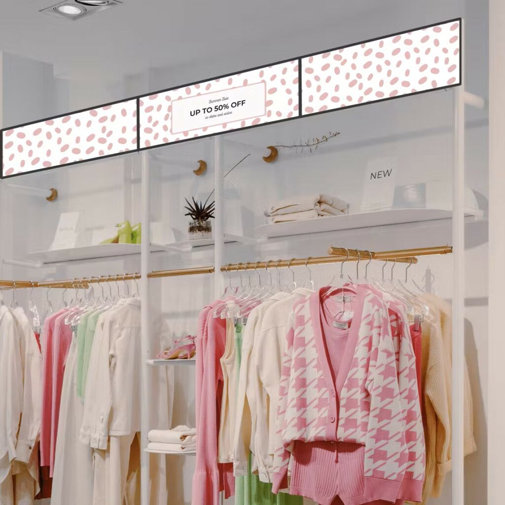 A set of three landscape digital screens above some clothes in a clothes shop.