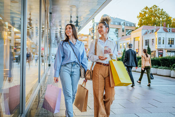 Young cheerful female friends looking at store windows while shopping together in the city.