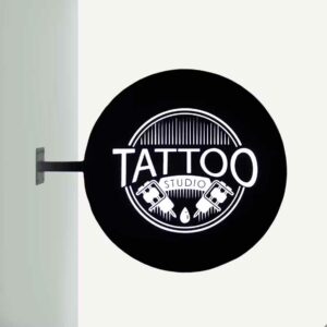 An outdoor illuminated lightbox sign with "tattoo" written on.