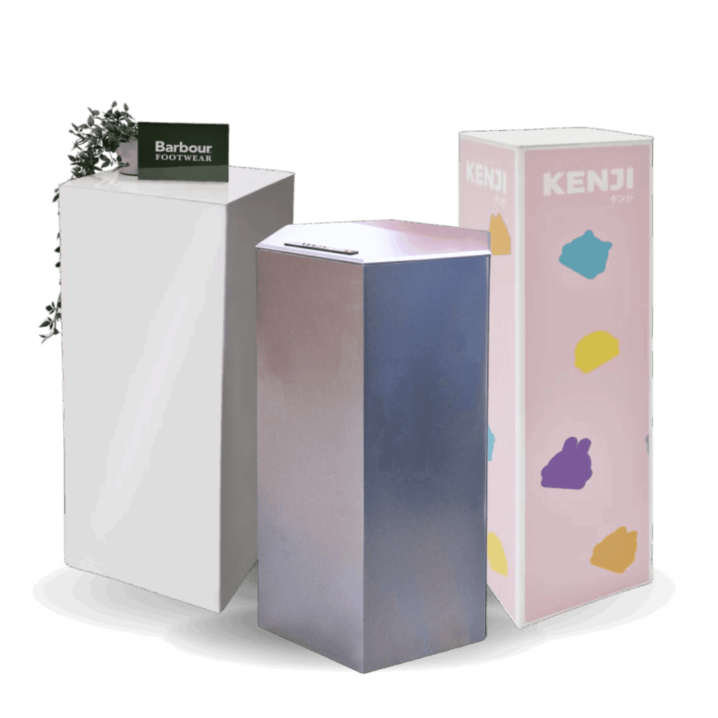 Three display plinth pedestals. One pink branded plinth, one white acrylic plinth & one custom branded metallic hexagonal plinth.