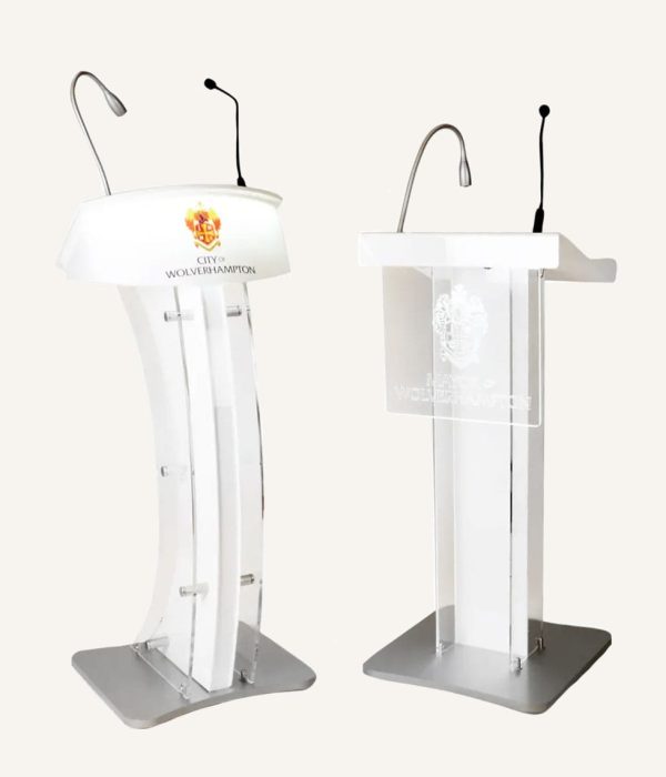 Two acrylic lecterns with silver and black microphones and logos on the front of them.